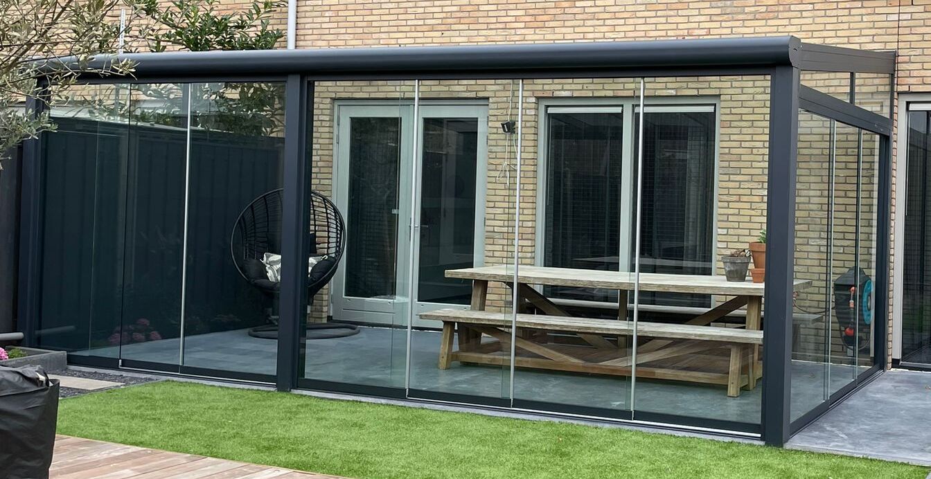 Standaard maten overkapping met aflopend dak aan nieuwbouw woning uitgevoerd in antraciet kleur en inclusief glaswanden te gebruiken als tuinkamer